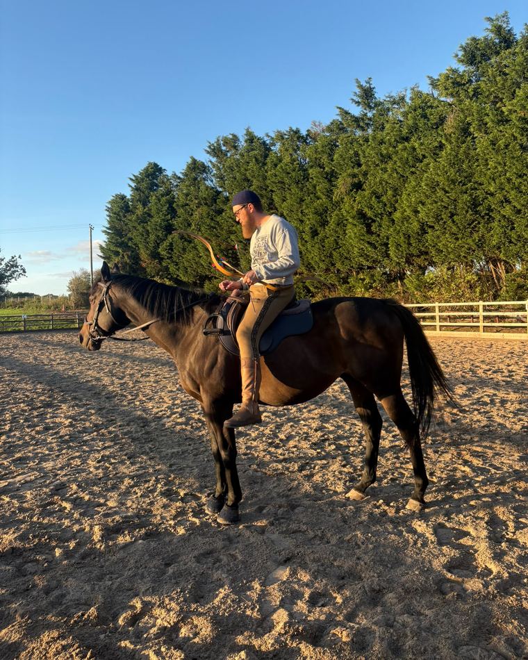 A rider holding a traditional horsebow on horseback in the arena
